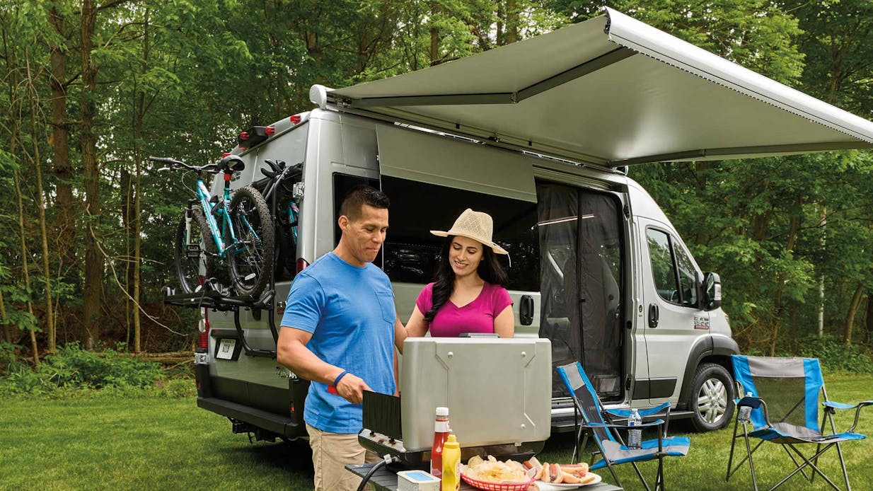 2022 Thor Rize Class B RV Camper Van Lifestyle couple grilling together with Thule® bike rack on rear door