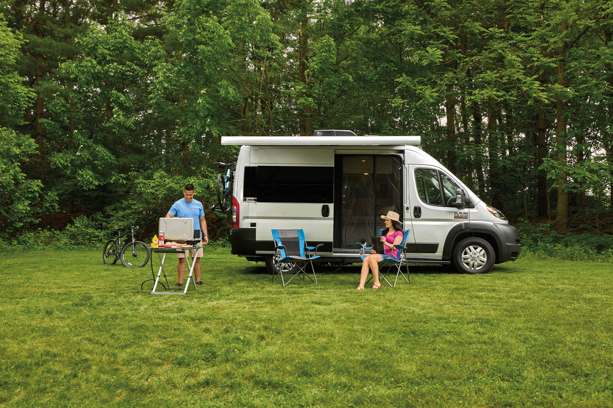 Thor Rize Class B Camper Van with family grilling outside surrounded by trees