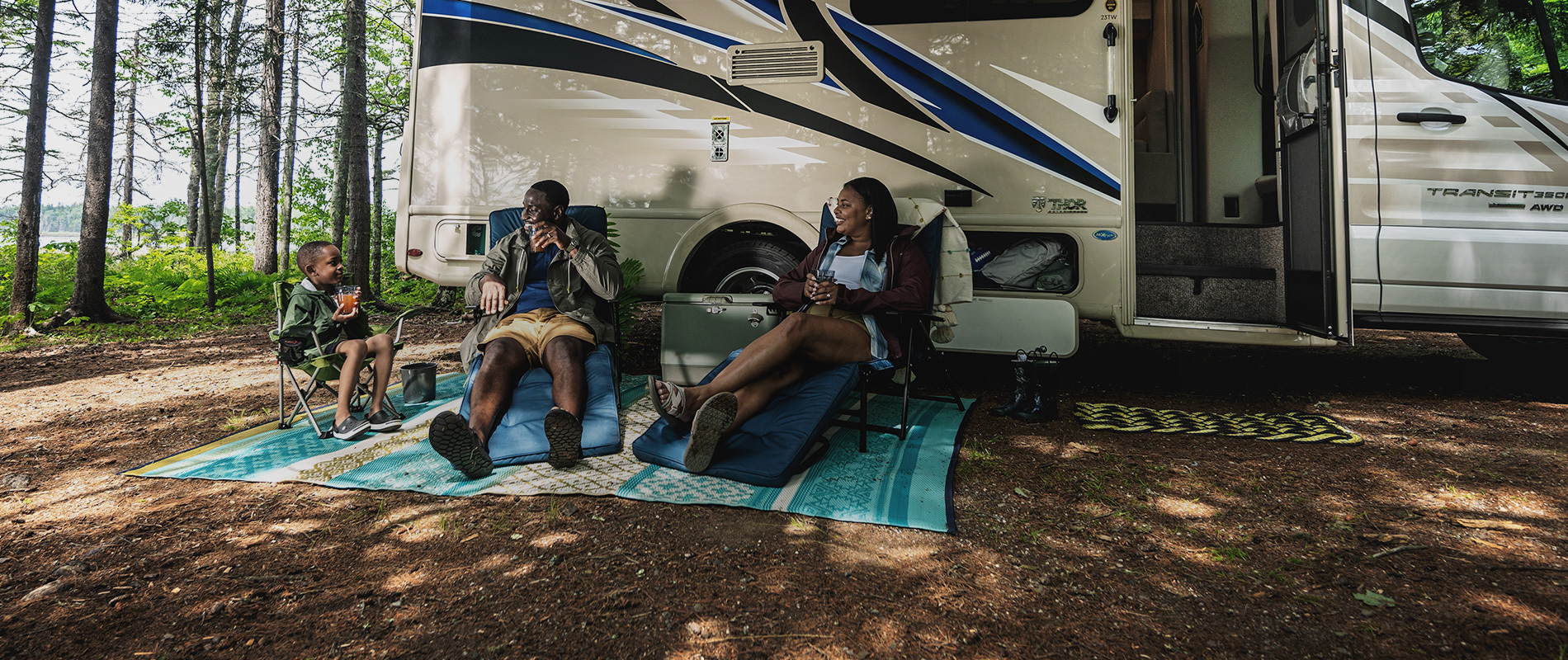 A family smiling at each other while sitting in the shade outside of their RV
