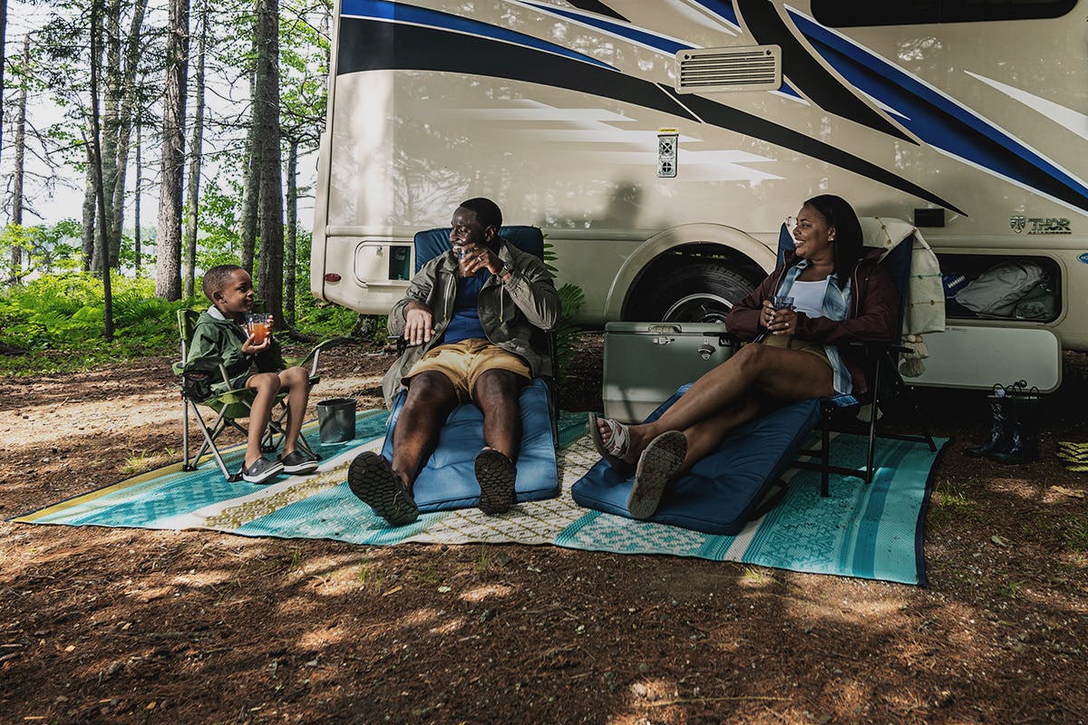 A family smiling at each other while sitting in the shade outside of their RV