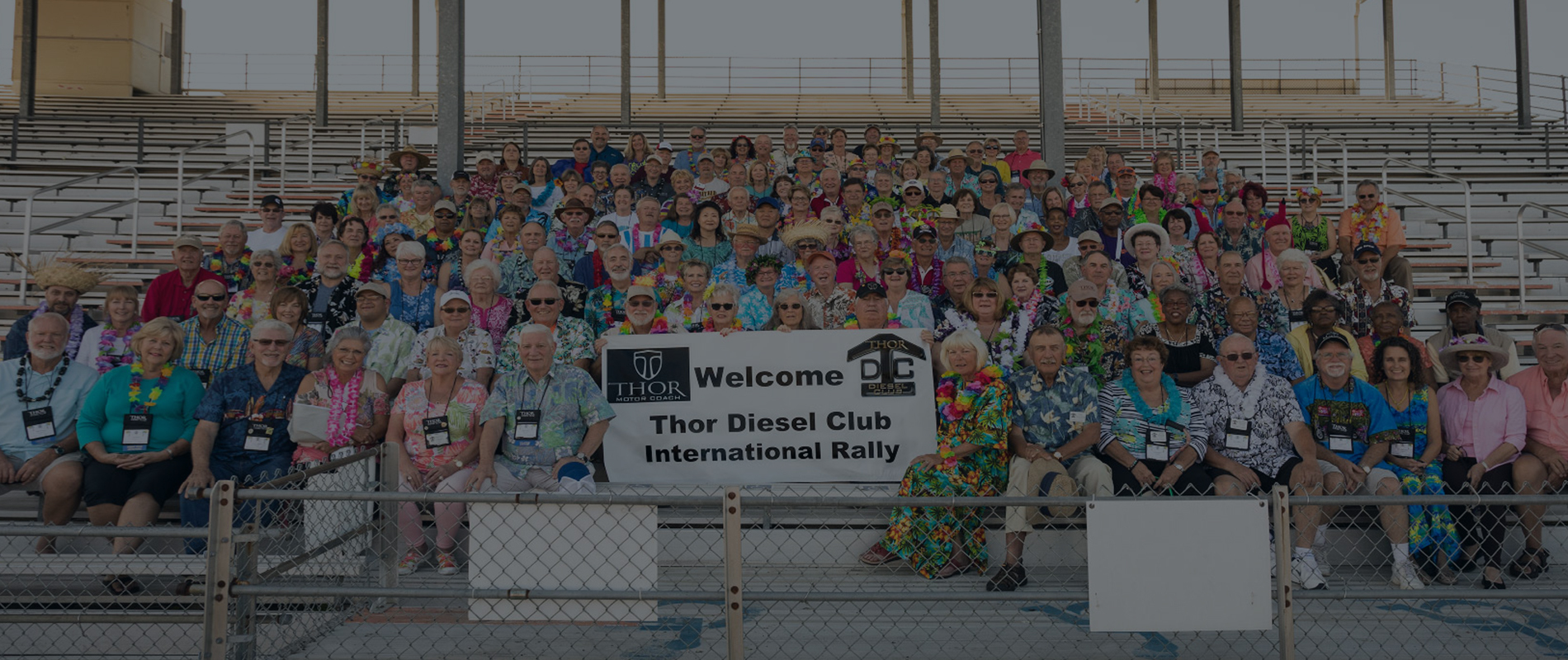 A group of motor coach owners sitting together with a large sign that says welcome Thor diesel club