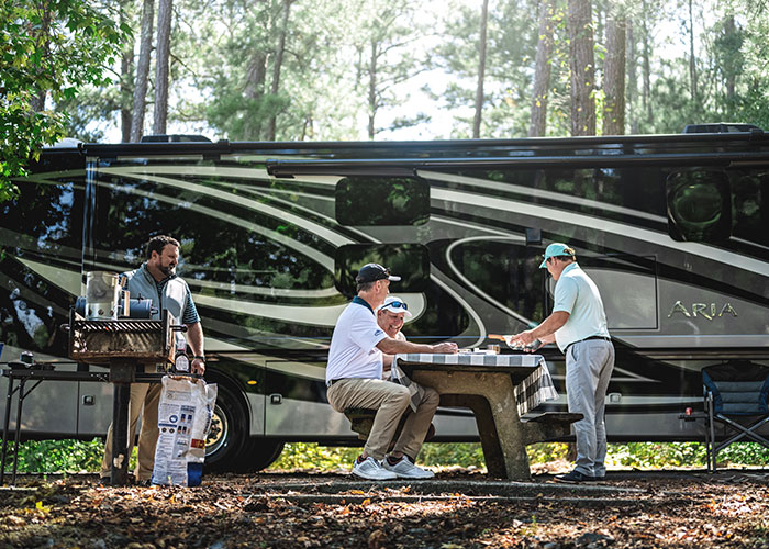 2021 Thor Aria Class A Diesel Pusher RV Lifestyle side view men grilling and eating at campsite