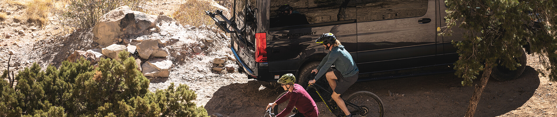 Two bicycle riders passing by their parked sanctuary sprinter van.